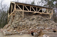 Die freigelegte Ruine der Pyramide mit Schutzdach. Ein Rampenverlauf zeichnet sich ab, unterhalb des Sockels zwei aufgebrochene Kammern. Blick von Osten (Aufnahme 2003)